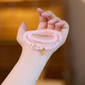 Détail d'un bracelet en cristal rose avec breloque cochon dorée et étiquette porte-bonheur