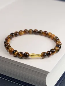 Macro detail of 6mm tiger eye beads with a golden matte fish charm on a book