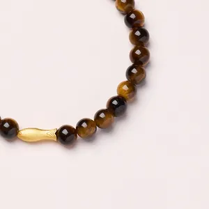 Detail of 6mm tiger eye stone bracelet with a textured golden fish bead charm