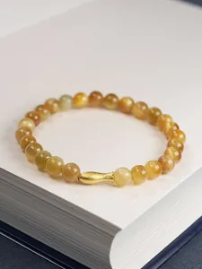 Macro shot of 6mm tiger eye beads and golden fish charm on an elegant white book