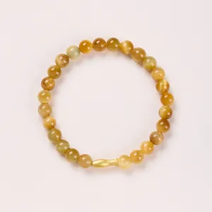 Macro detail of 8mm tiger eye beads and golden fish charm on a minimalist bracelet