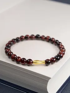 Close-up of 6mm red tiger eye bead bracelet with a matte golden fish charm detail
