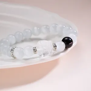 Détail d'un bracelet en cristal bleu pâle avec breloque pixiu sur une assiette en céramique