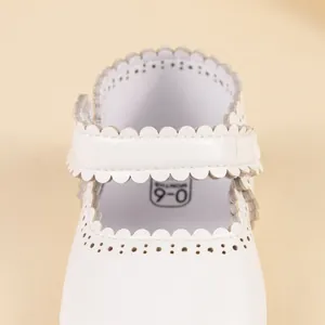 Dettaglio di scarpine baby in pelle bianca con bordo smerlato e marcatura taglia 0-6 mesi