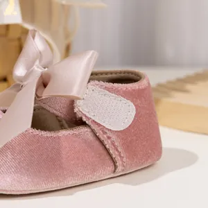 Close-up of pink velvet baby shoes with satin bow and velcro strap detail