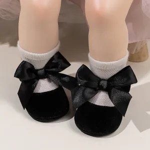 Close-up of black velvet baby princess shoes with satin bow and white knitted socks