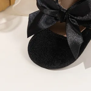 Close-up of baby Mary Jane shoes featuring black velvet material and large satin bow detail