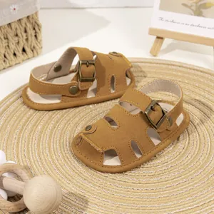 Brown suede baby sandals with cut-out toe design and buckle on a rustic straw mat