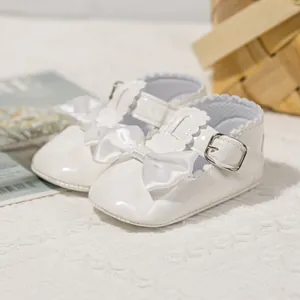 Detail von weißen Lackleder-Babyschuhen mit Satinschleifen und Wellenrand