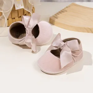 Close-up of pink velvet baby shoes with large satin ribbons on a rustic wooden tray