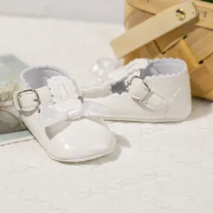 Detail von weißen Baby-Lackschuhen mit Satinschleifen und Wellenrand