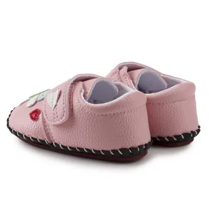 Detail view of pink leather baby shoes with heart patch and white stitching on brown soles