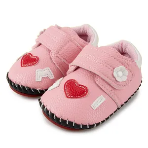Détail de chaussures bébé roses avec écusson cœur, bride Velcro et cuir synthétique grainé