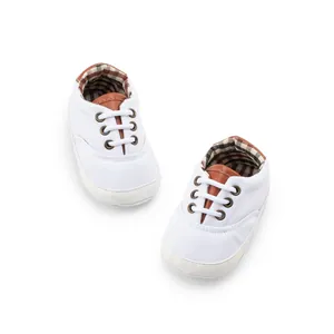 Macro detail of white baby canvas shoes with brown trim and plaid inner lining