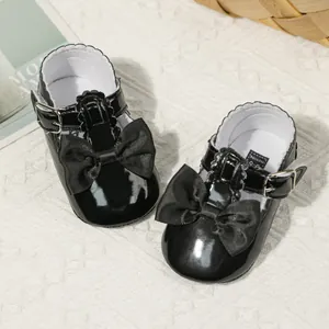 Detail von schwarzen Lackleder-Babyschuhen mit Satinschleife und T-Riemen-Verschluss