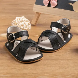 Detail of black infant sandals with cross straps and silver buckle on wood surface