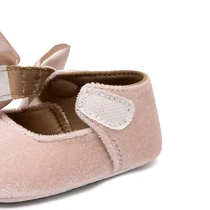 Detail of pink velvet baby Mary Janes featuring a satin bow and velcro strap