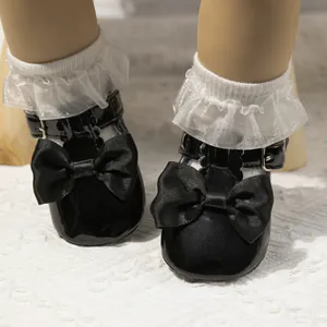 Nahaufnahme glänzender schwarzer Lack-Babyschuhe mit großer Seifenschleife und Socken