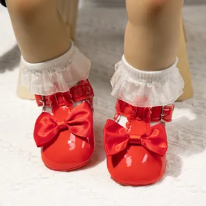 Detail von glänzenden roten Babyschuhen aus Lackleder mit großer Satinschleife