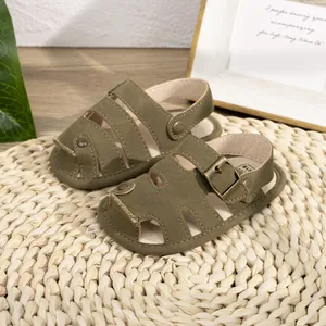 Olive green closed-toe PU leather baby sandals with adjustable buckles on a natural mat