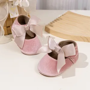Pink velvet baby walker shoes with large satin bows displayed on a wooden tray