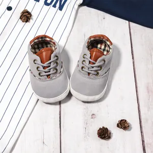 Grey canvas baby walking shoes with soft soles and brown trim on a wooden background