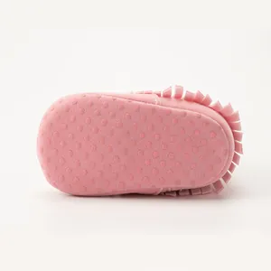 Macro view of pink suede baby shoes with anti-slip rubber dots and tassel details