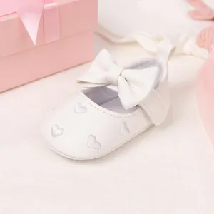 Detail of white baby walking shoe with silver heart embroidery and large bow decoration