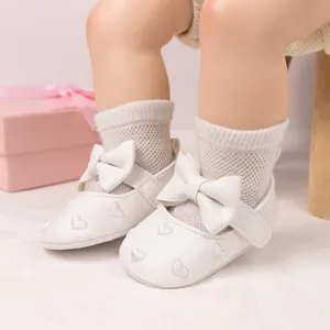 Detailed macro view of white leather baby shoes with bow and heart embroidery