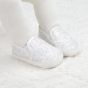 Silver glitter baby slip-on shoes with soft soles shown on a white knitted rug