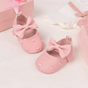 Detail of pink baby princess shoes featuring a large bow and heart embroidery