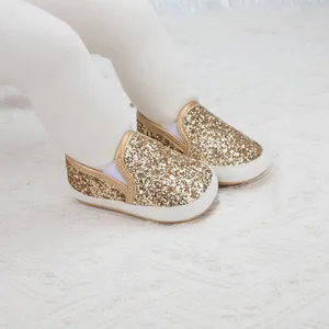 Close-up of golden sequin baby walker shoes with elastic bands on a white knit blanket