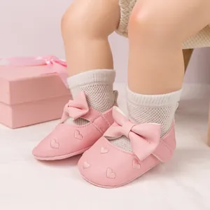 Detail of pink baby shoes with big bow and heart embroidery on a soft sole model