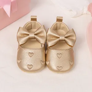 Detailed view of golden baby Mary Jane shoes with embossed heart patterns and bow