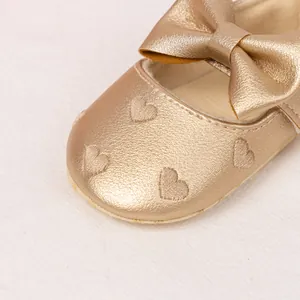Detail of gold Mary Jane baby shoes with heart embroidery and large bow decoration