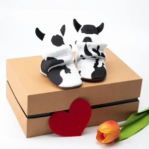 Cute cow pattern baby booties with soft soles and horns shown on a gift box