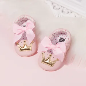 Pink baby walking shoes with ribbon bow and gold crown on white plush background