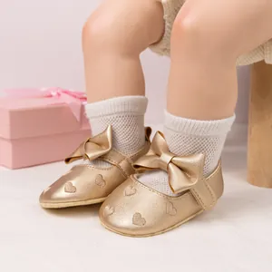 Detail of baby princess shoes in gold leather with heart embossing and large bow