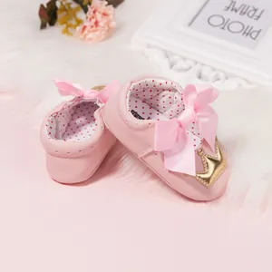 Pink princess baby walking shoes with silk bow and gold crown on white plush mat