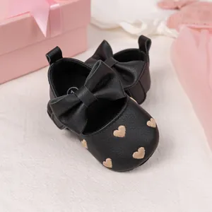 Detail of baby girl shoes in black faux leather with heart embroidery and bow on gift box