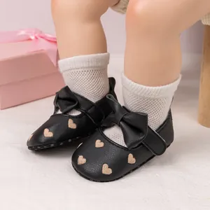 Close-up of black baby princess shoes with gold heart embroidery and large bow