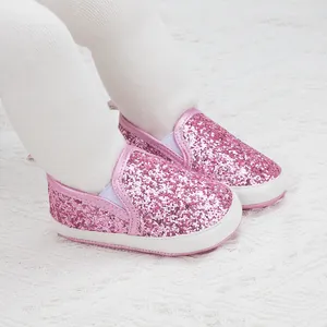 Detail of pink sequin baby loafers on a lace surface featuring a slip-on design