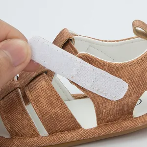 Λεπτομέρεια του ρυθμιζόμενου ιμάντα velcro σε καφέ υφασμάτινα βρεφικά πέδιλα