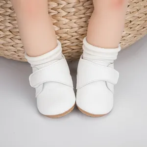 Gros plan d'une chaussure bébé blanche à scratch sur fond en paille naturelle