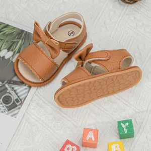 Detailed view of brown baby sandals featuring a large bow and scalloped edge detail