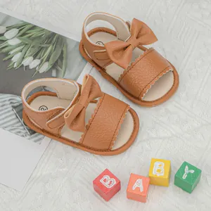 Detail of brown leather baby sandals featuring a large bow and scalloped edges