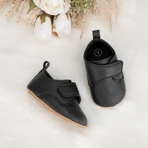 Chaussures bébé en cuir noir avec semelles souples et velcro sur un fond en peluche
