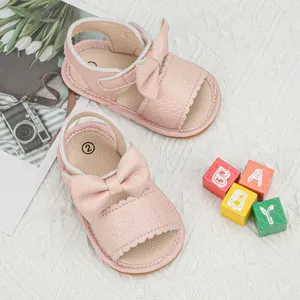 Detail of pink leather baby sandals featuring a bow decoration and scalloped edges