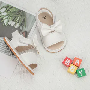 Close-up of white baby girl sandals with litchi texture and large leather bow detail