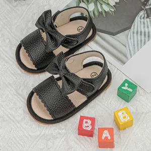 Detail of black leather baby sandal with bow decoration and scalloped edges on white knit